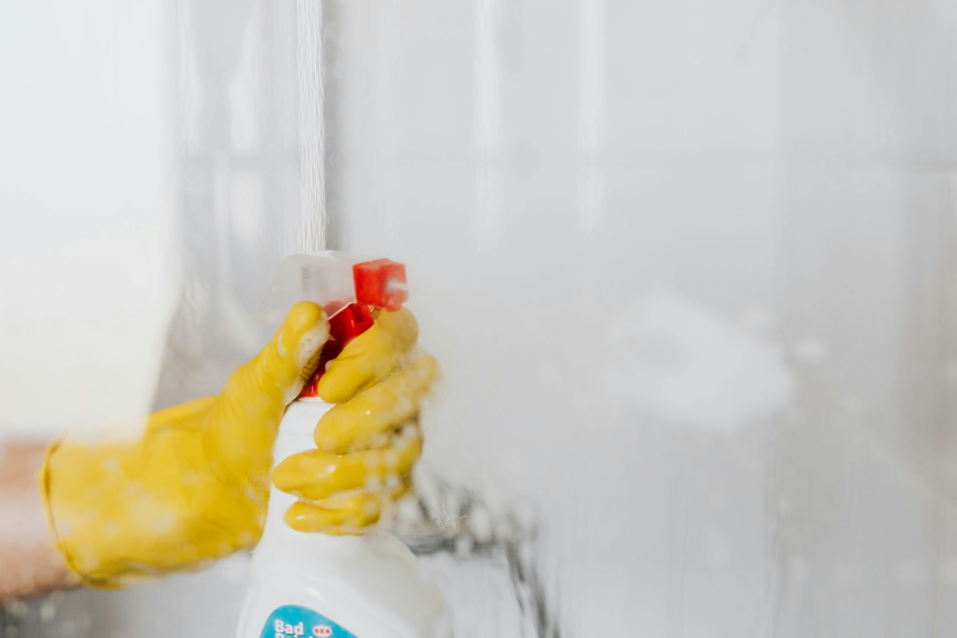Yellow-gloved hand sprays cleaner on a glass surface