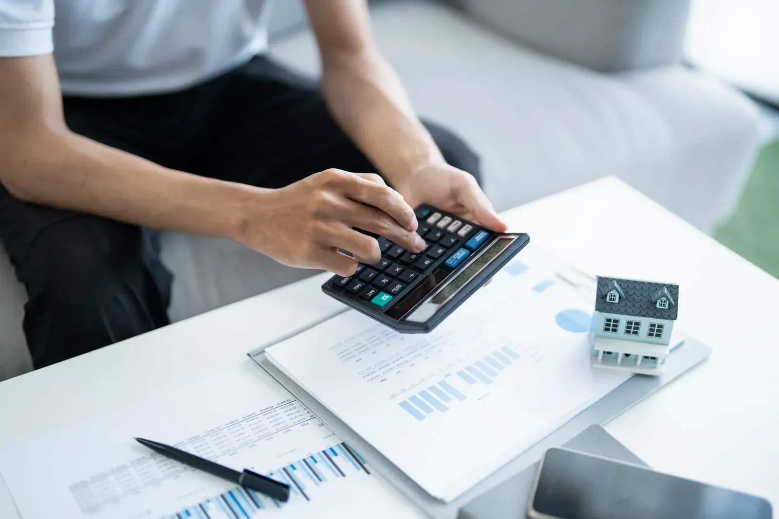 Person using a calculator over financial documents on a desk with charts and a pen