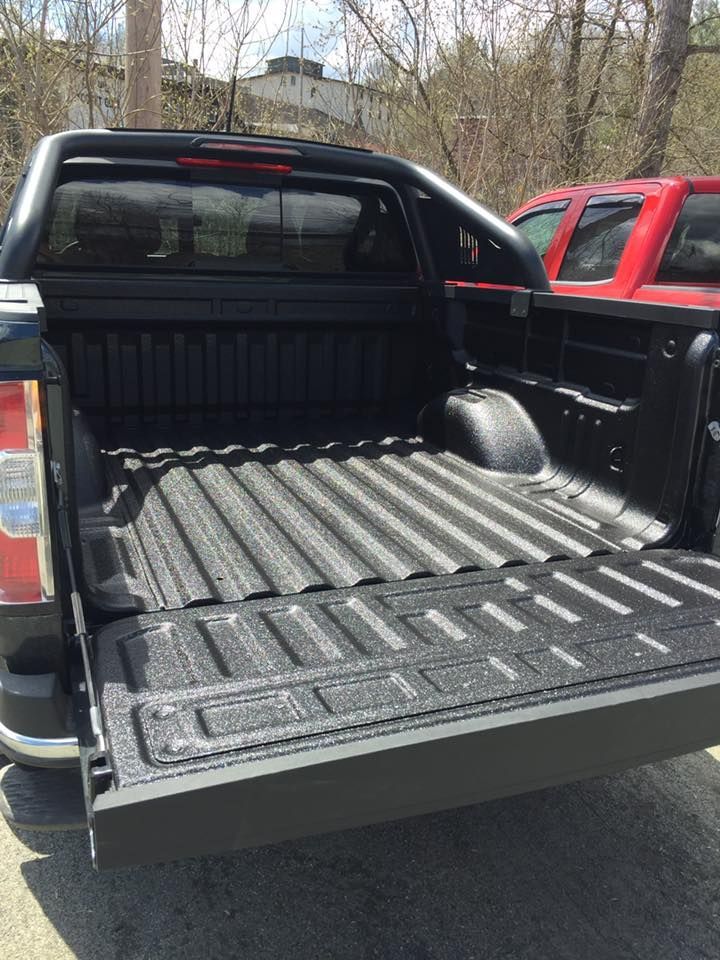 A black truck with the bed open showing the spay in bedliner is parked next to a red truck.