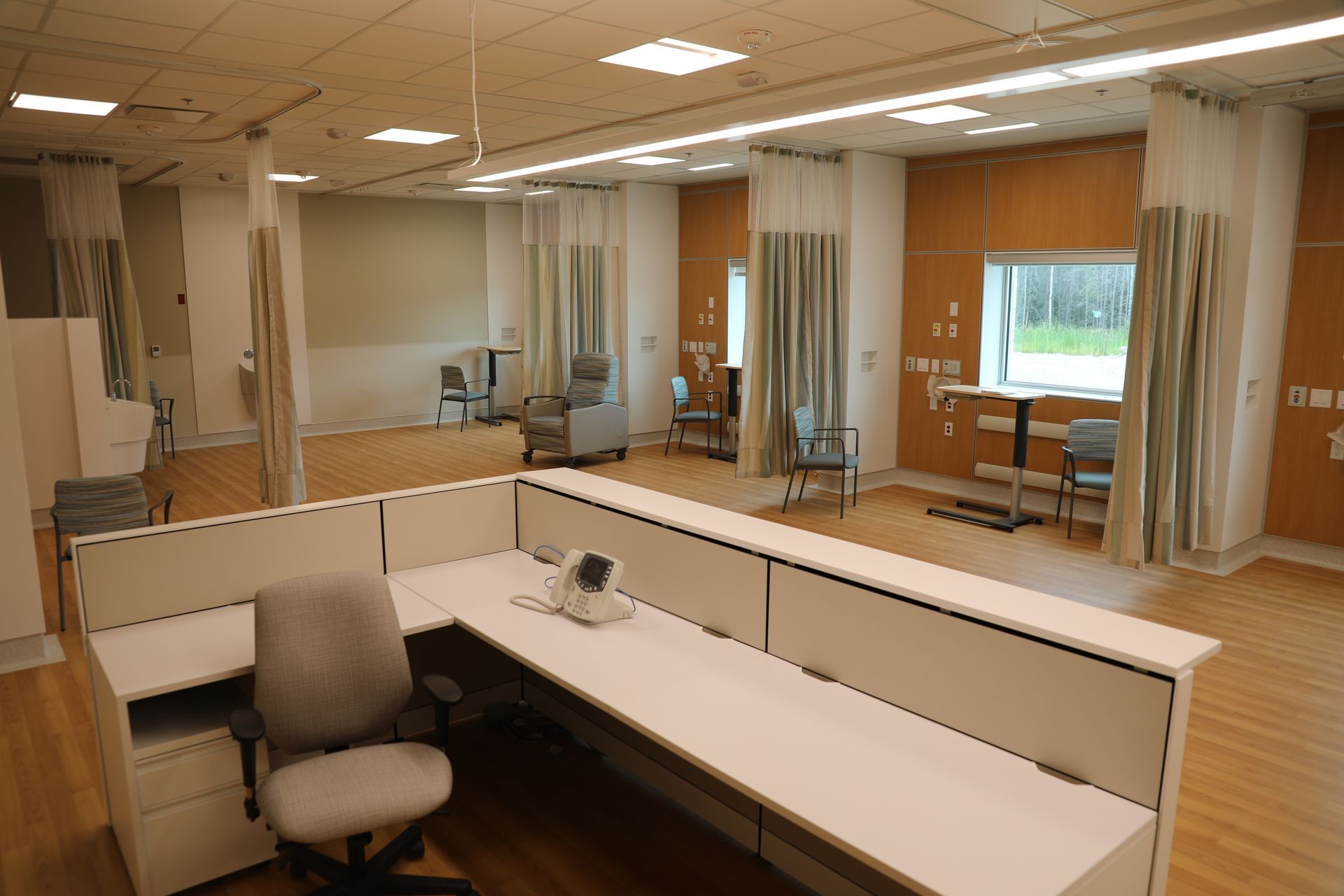 A cubicle in a hospital with a desk and chairs.