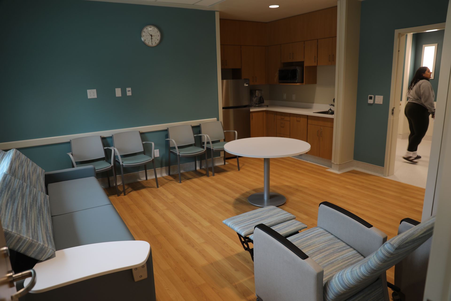 A living room with a couch , chairs , a table and a clock on the wall.