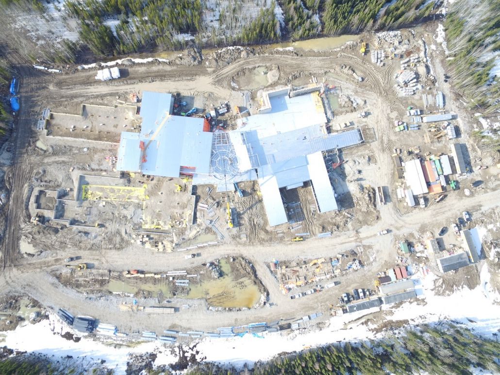 An aerial view of a building under construction in the middle of a snowy forest.