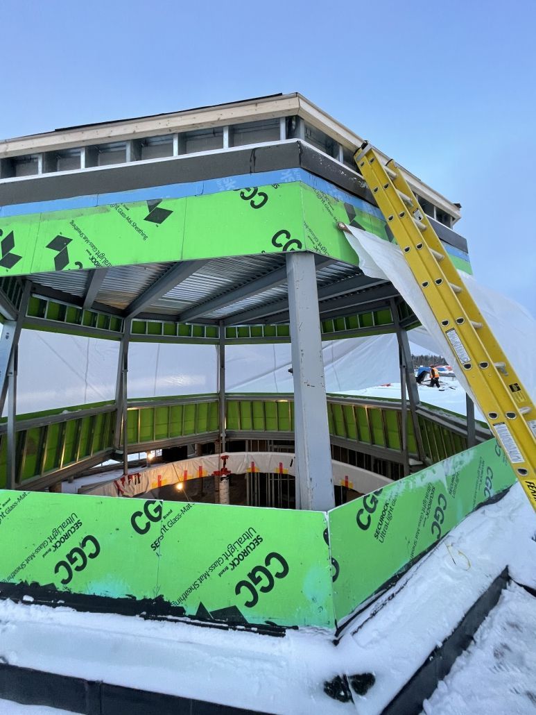 A gazebo is being built in the snow with a yellow ladder