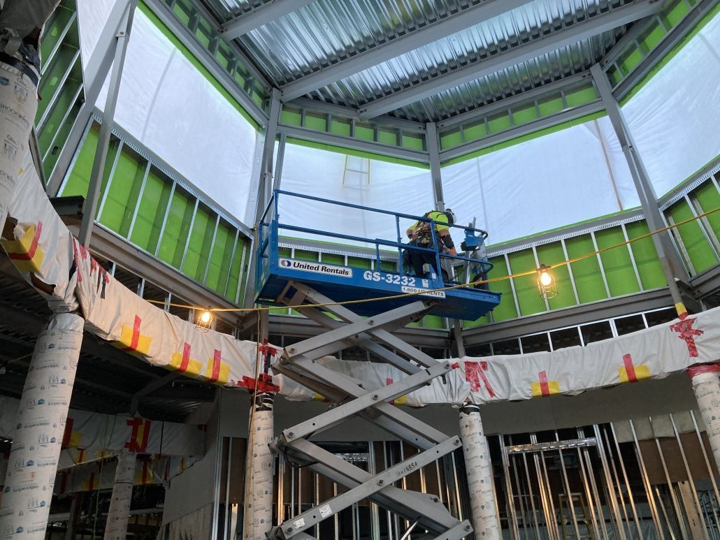 A man is standing on a scissor lift in a building under construction.