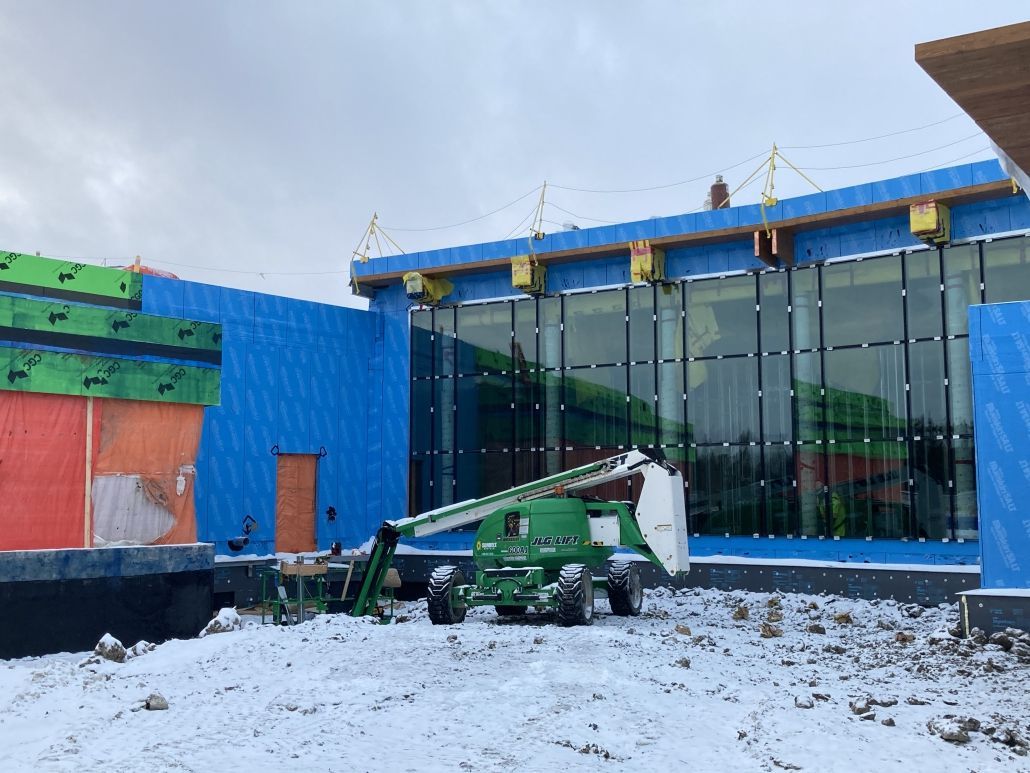A green crane is parked in front of a building under construction.