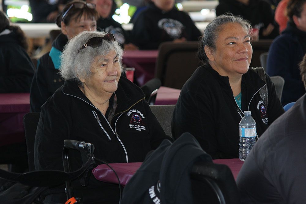 Two older women are sitting at a table with a bottle of water