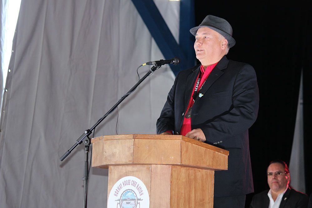 A man in a suit and hat stands at a podium speaking into a microphone