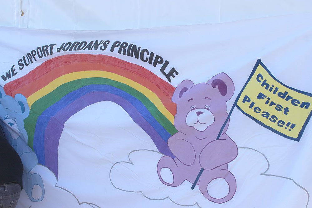 A teddy bear holding a sign that says children first please