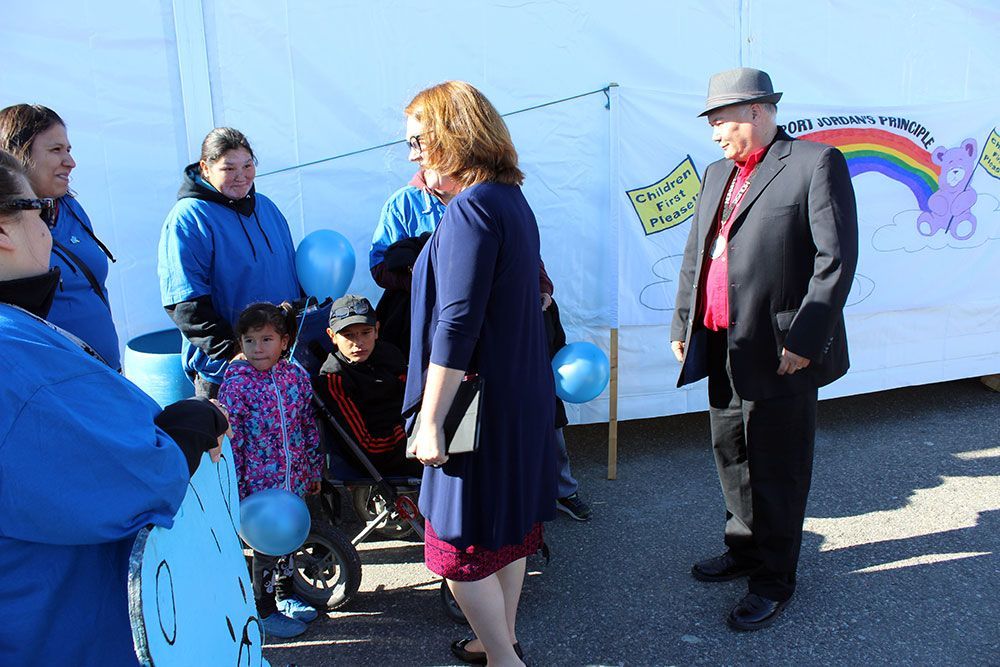 A group of people are standing in front of a white wall with a rainbow on it.