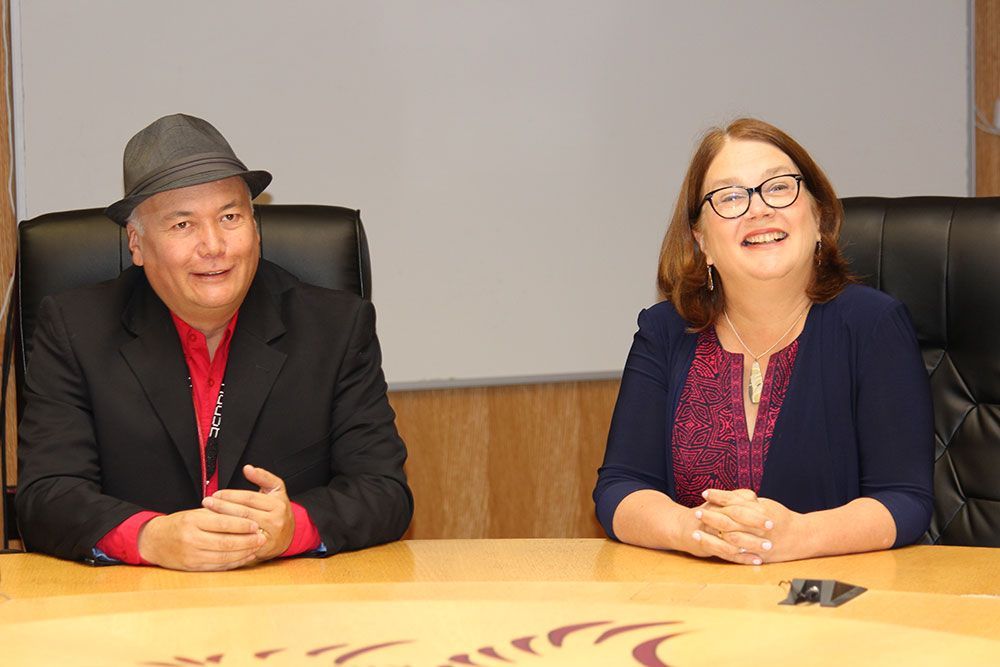 A man and a woman are sitting at a table with their hands folded.