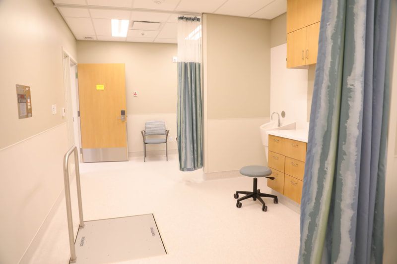 A hospital room with a blue curtain and a chair