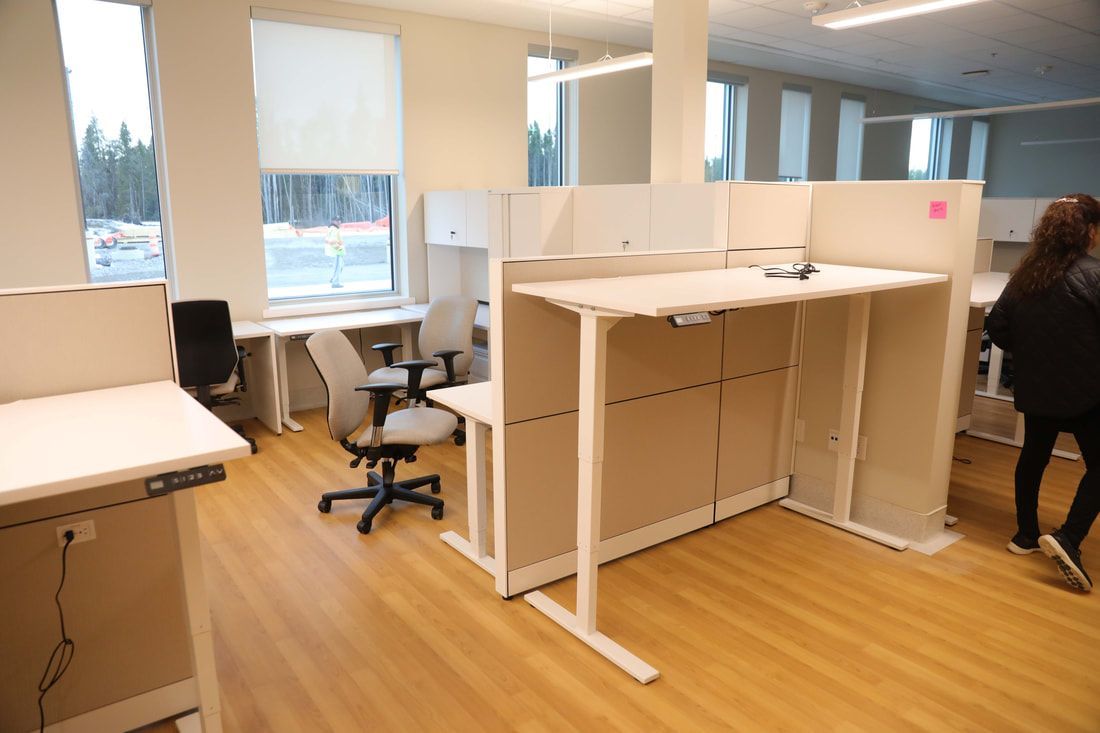 A woman is standing in a room with a lot of desks and chairs.