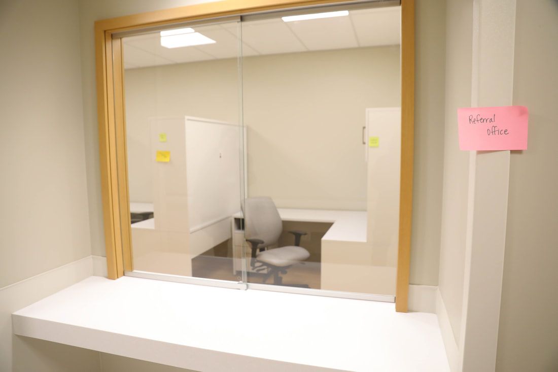 A room with a desk and chair and a window with a pink sign that says first aid on it.