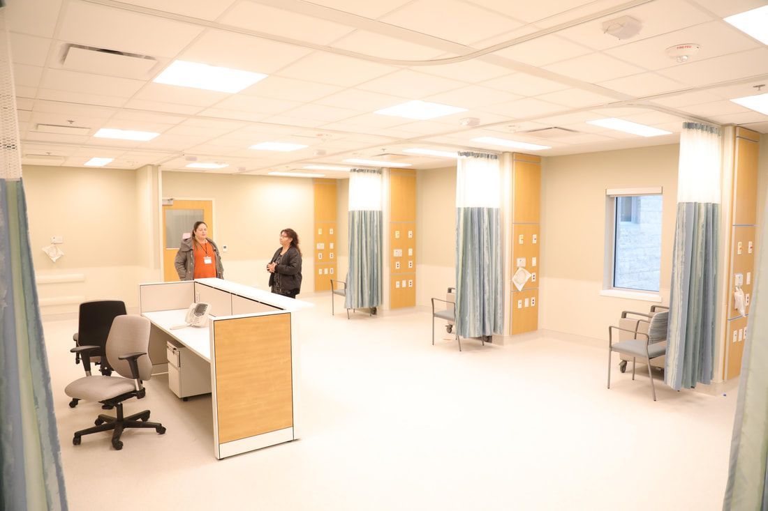 Two people are standing in a hospital room with blue curtains.