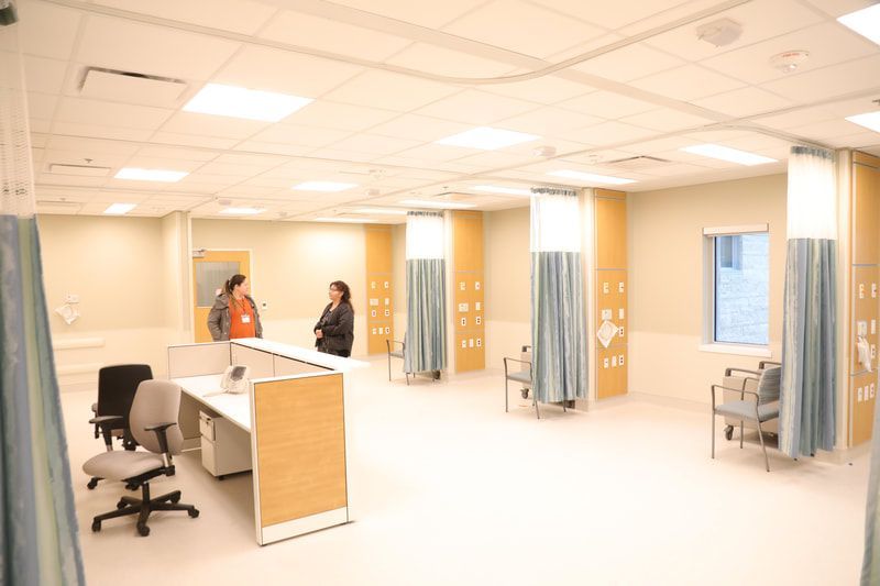 Two women are standing in a hospital room talking to each other.