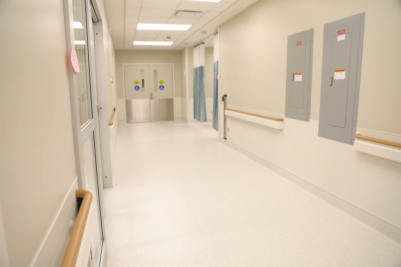 An empty hospital hallway with white floors and wooden handrails.