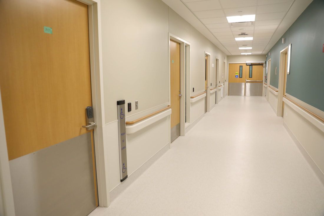 An empty hospital hallway with wooden doors and a white floor.