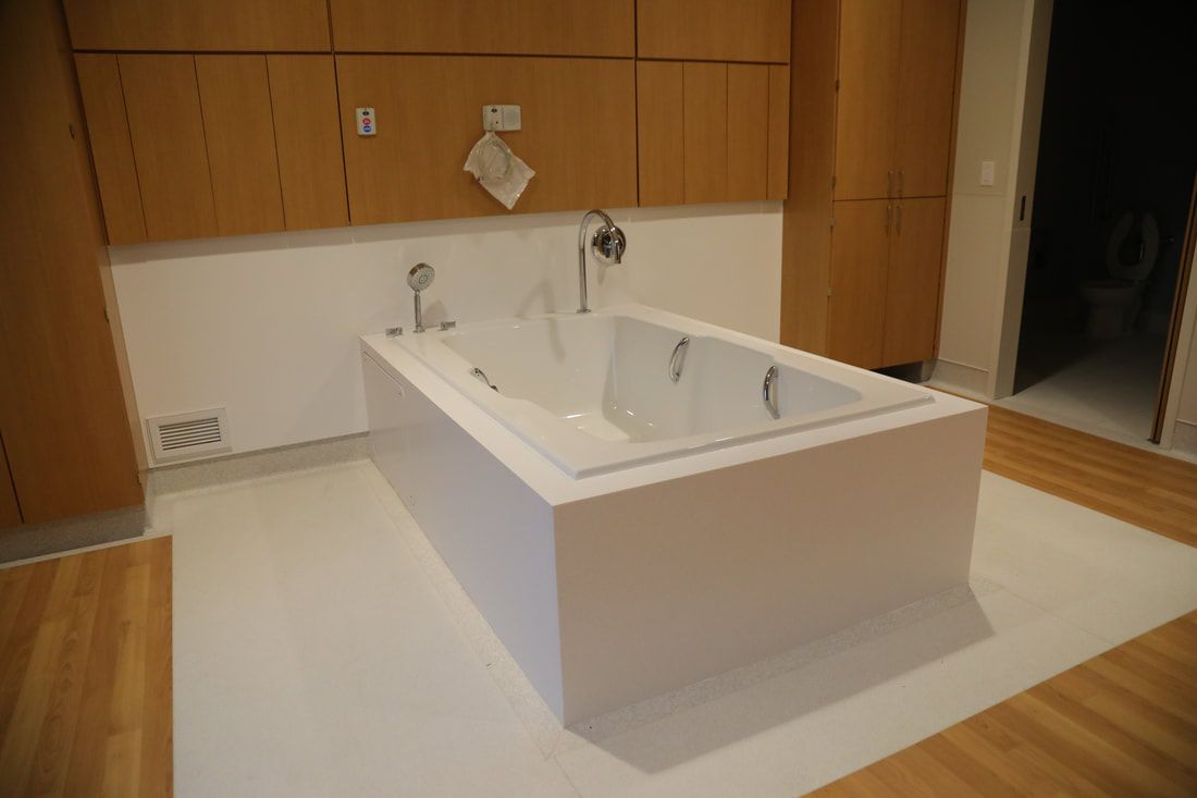 A large white bathtub is sitting on a wooden floor in a bathroom.