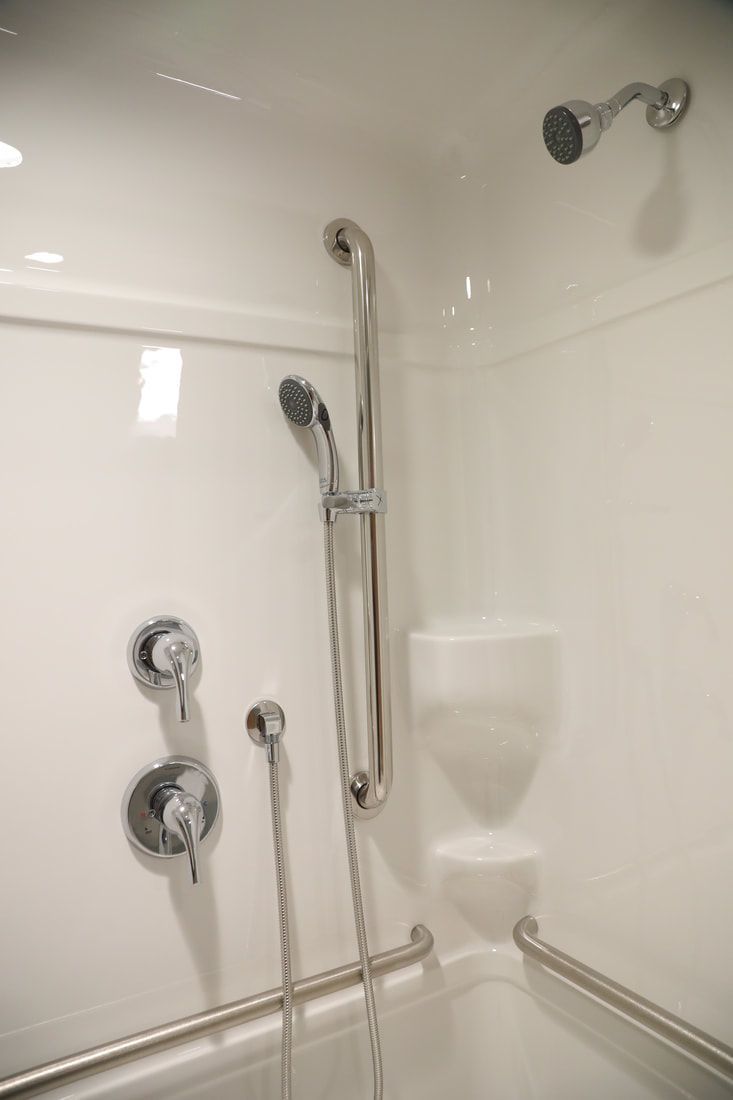 A bathroom with a shower , tub , and handrails.