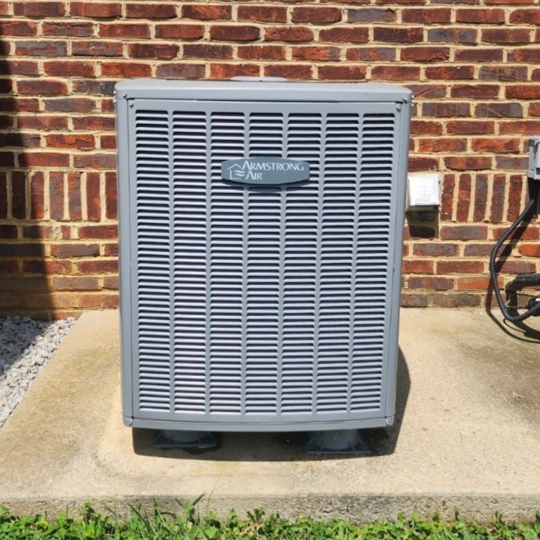 A gray air conditioner is sitting in front of a brick wall