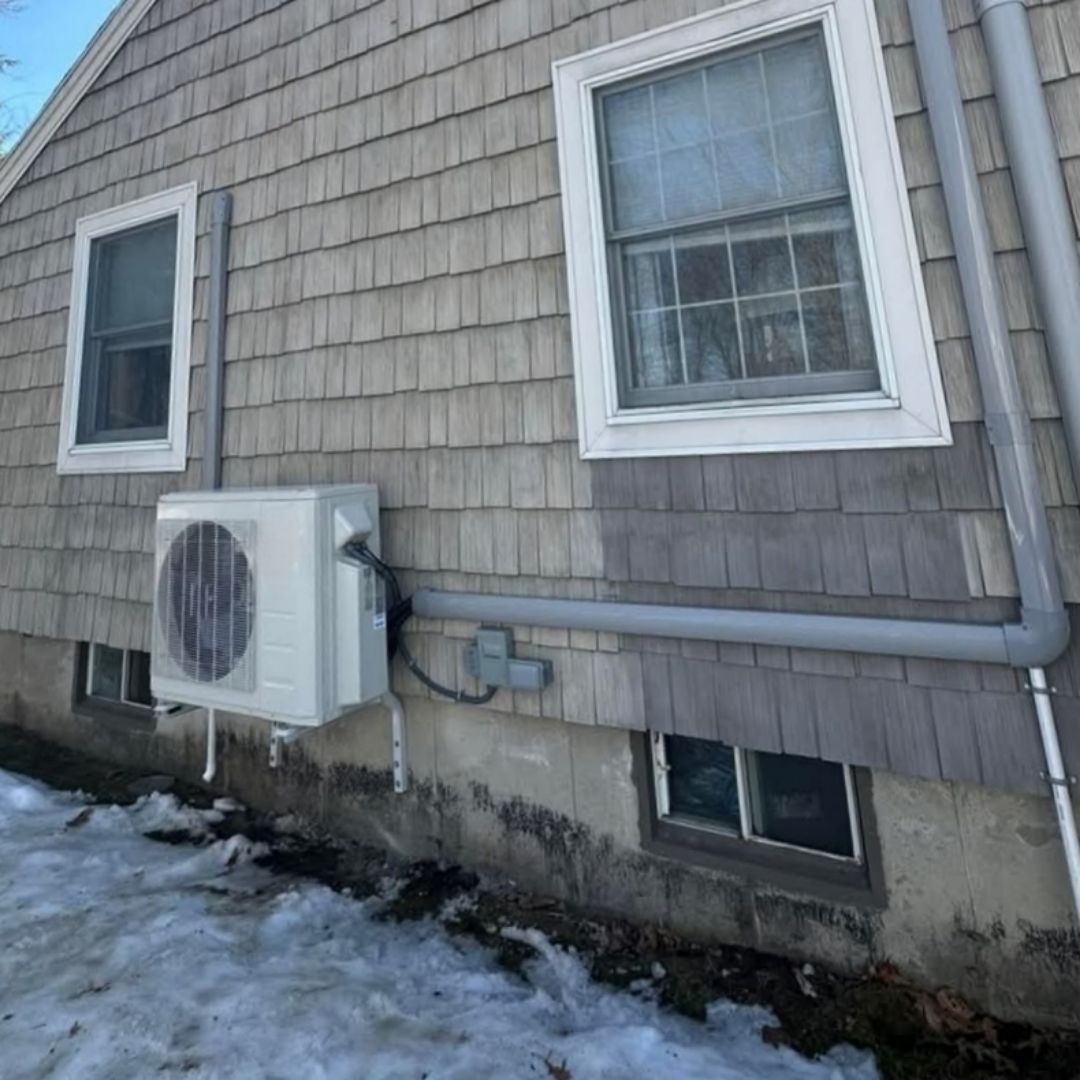 A white air conditioner is attached to the side of a house.