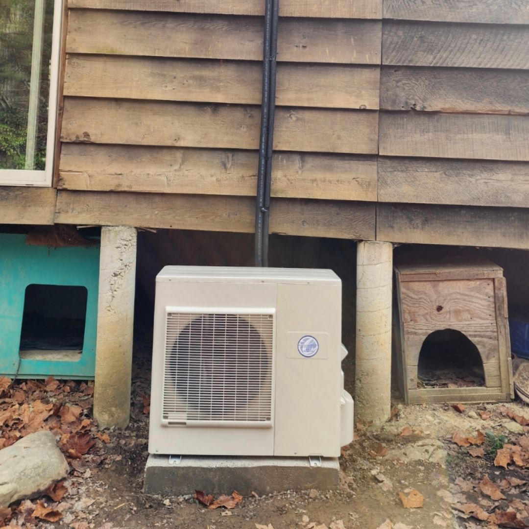 A white air conditioner is sitting in front of a wooden building