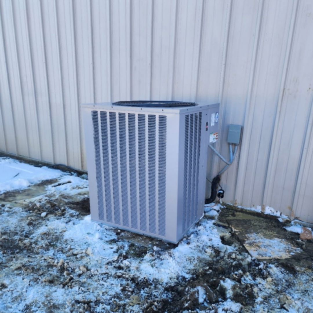 A large air conditioner is sitting outside of a building in the snow.