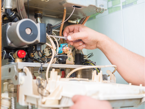 A person is fixing a boiler with a wrench.