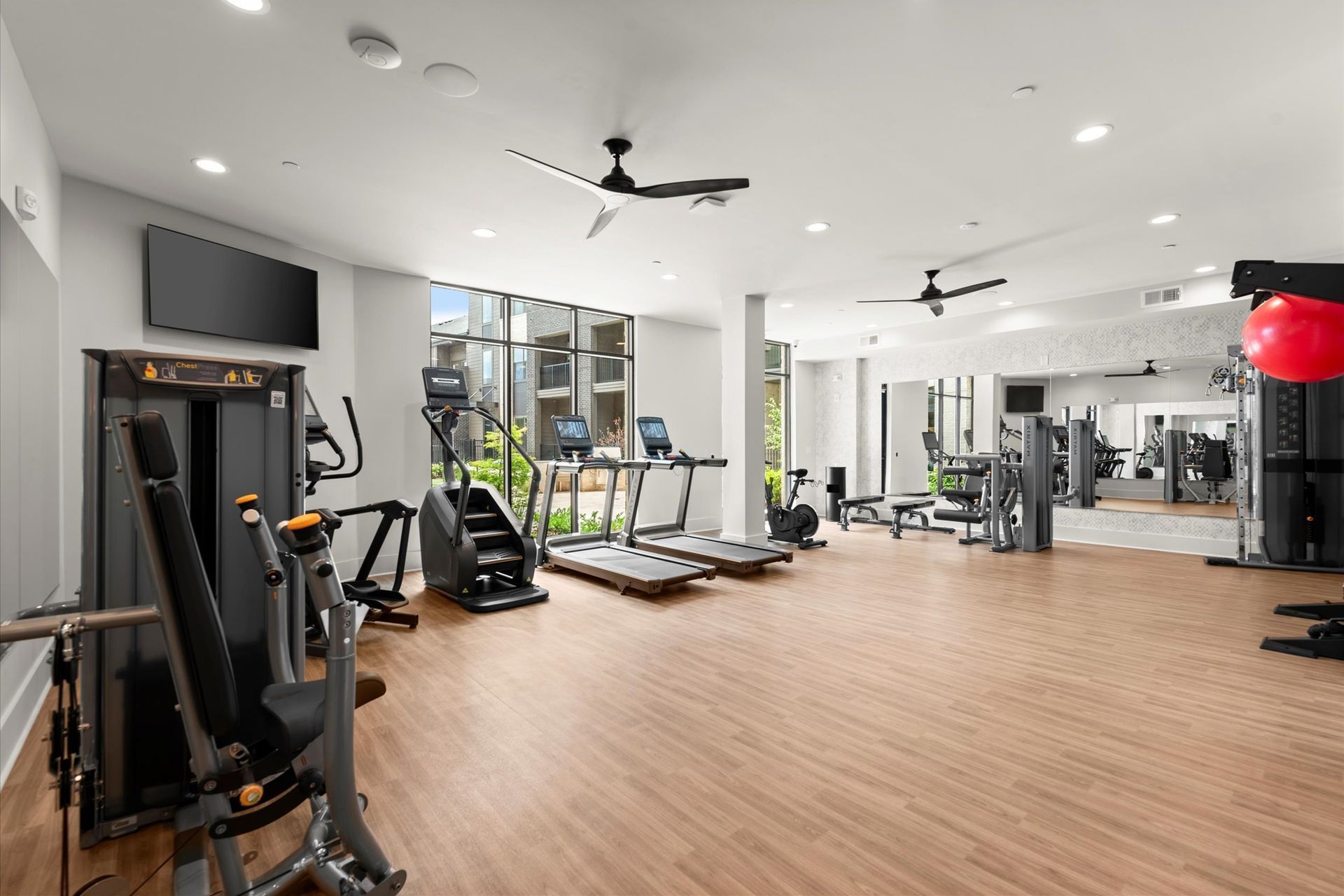 Gym with exercise equipment, including treadmills, stair stepper, and weight machines, with large windows.