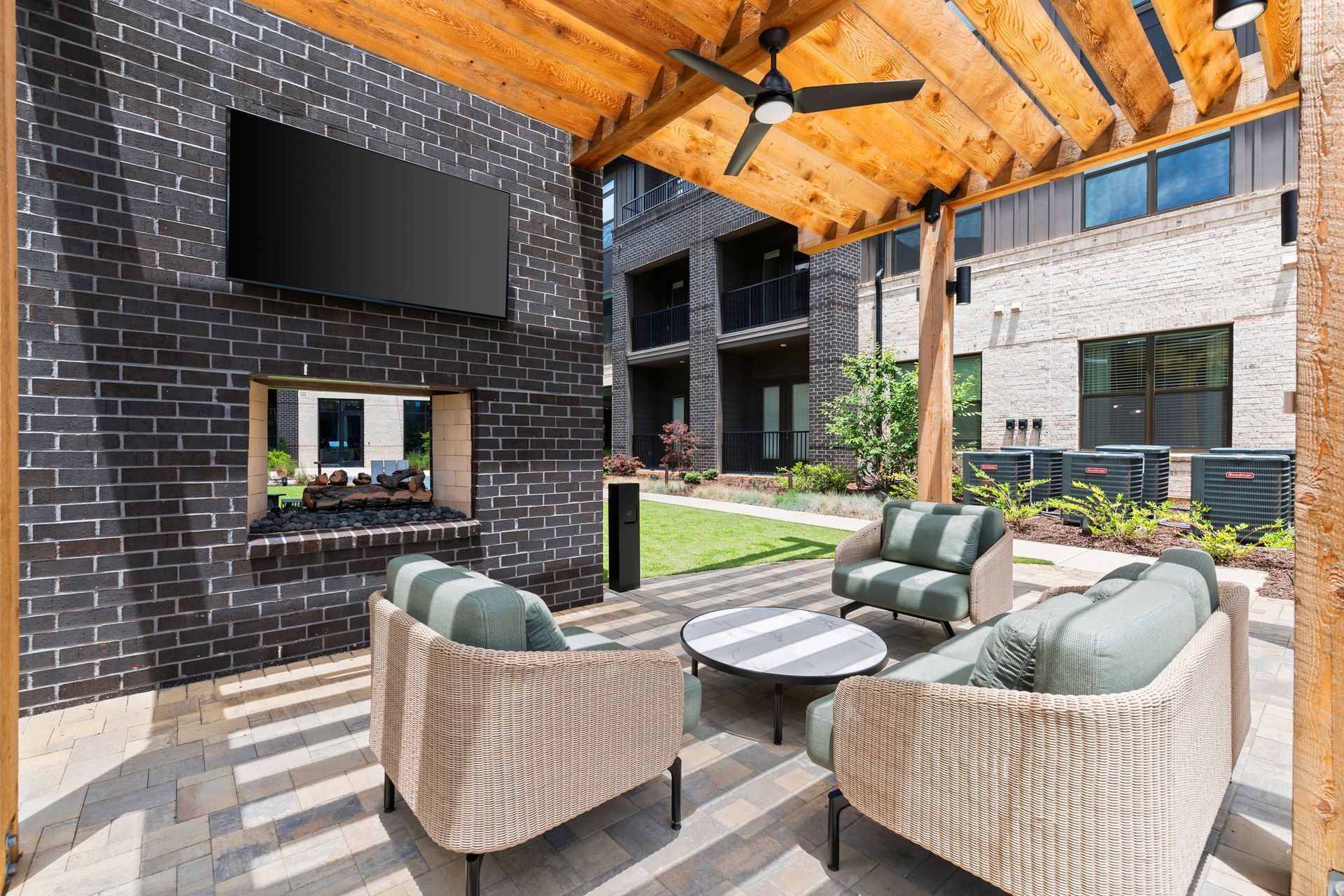 Outdoor lounge area with seating, fireplace, TV, and overhead wooden structure.