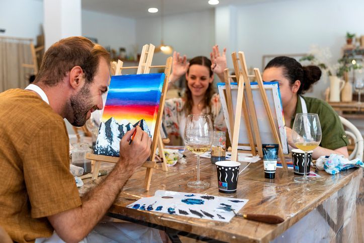People painting at easels in an art studio, one person smiles at their canvas.