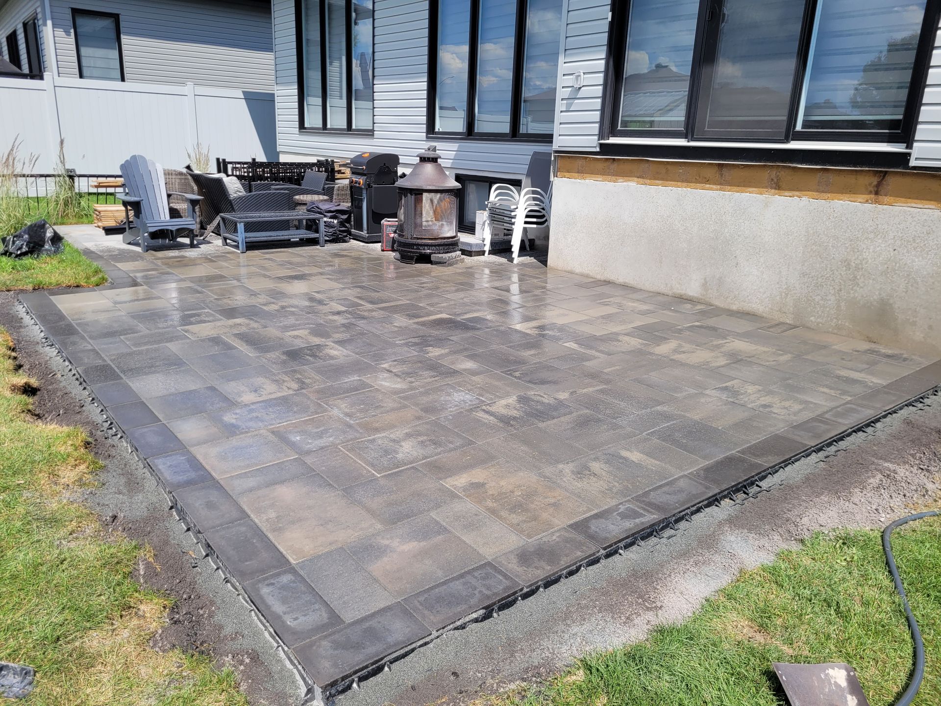 Newly constructed patio with dark pavers and a dark border. A house is in the background.
