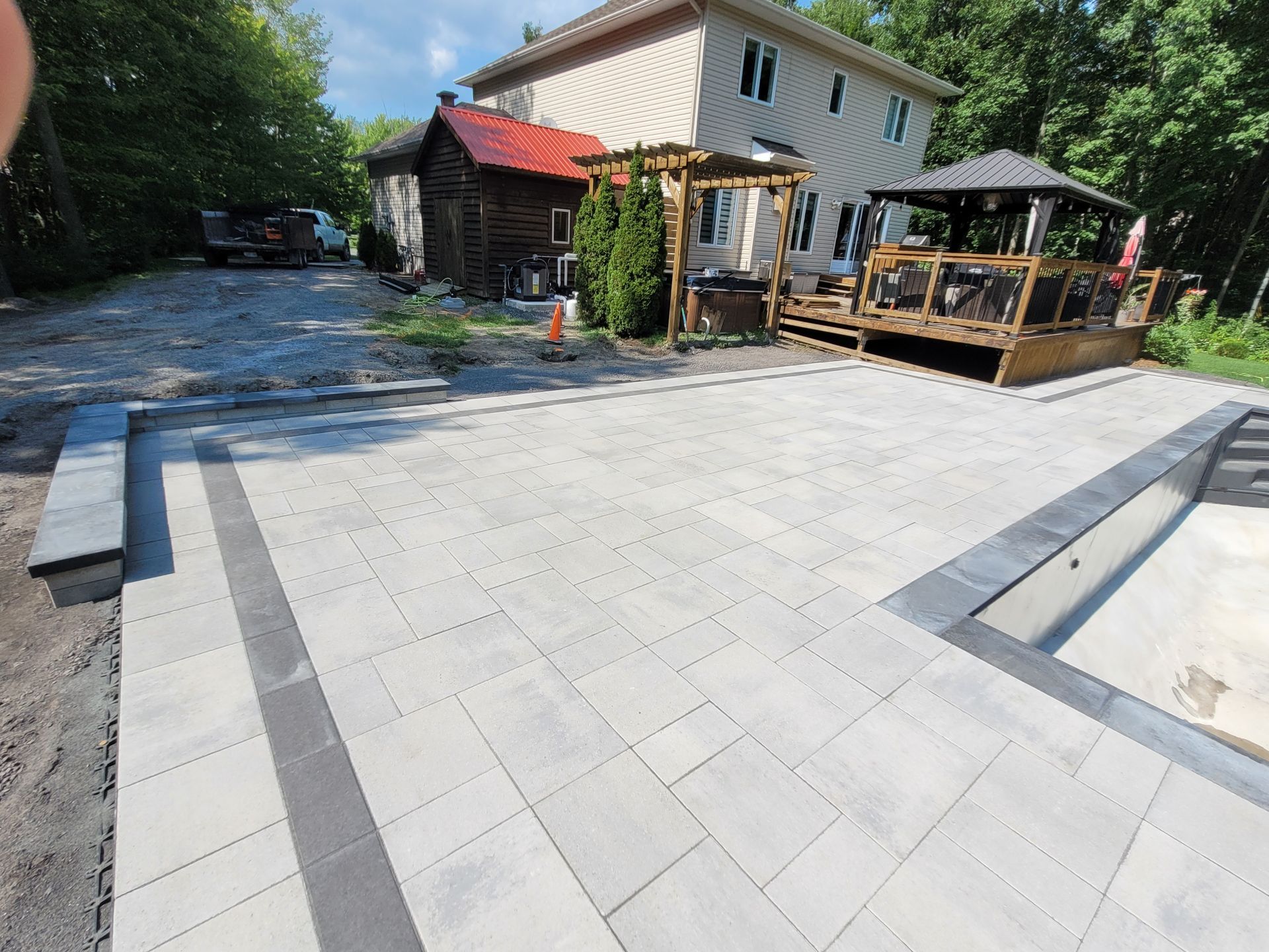 Backyard patio with gray pavers, pool, deck, and house.
