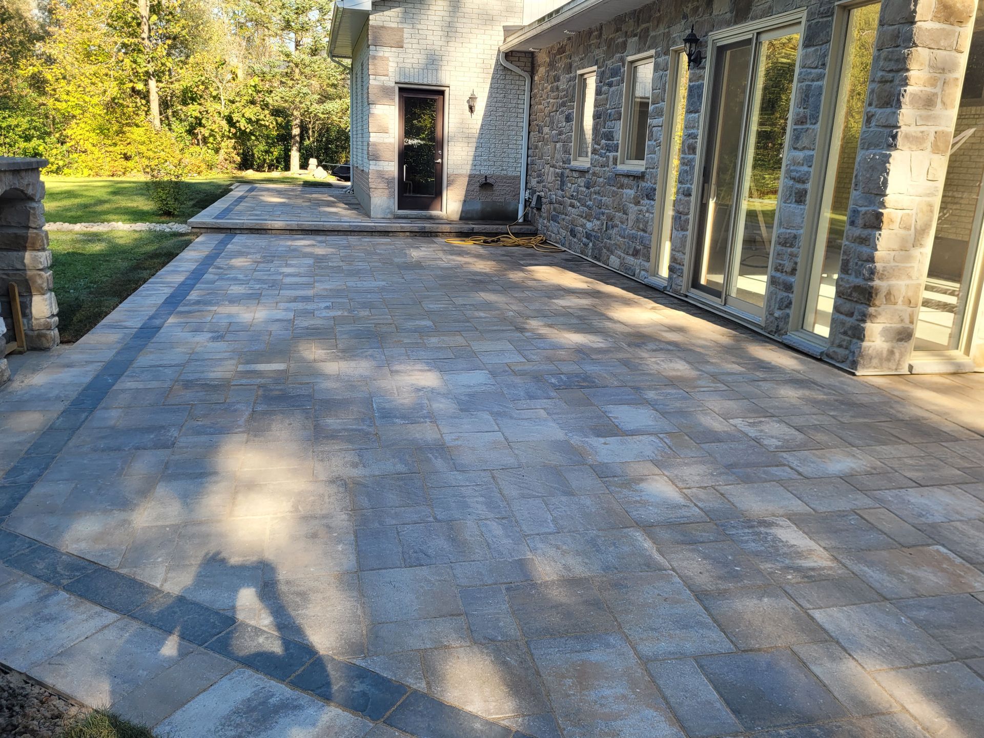 Stone patio next to a house with large windows and a dark door.