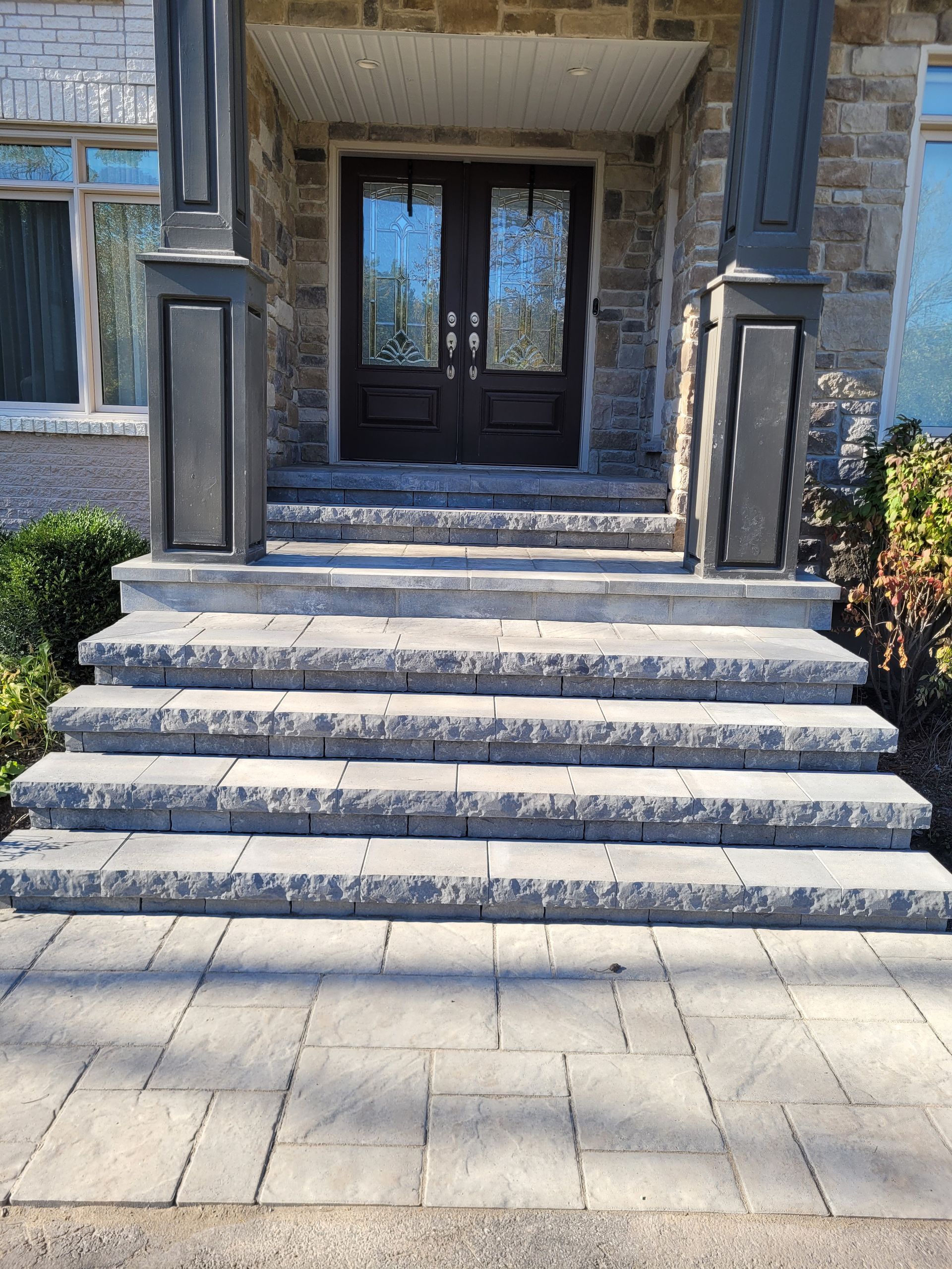 Stone steps leading to a front door with glass panels. Gray steps and pathway, flanked by columns.