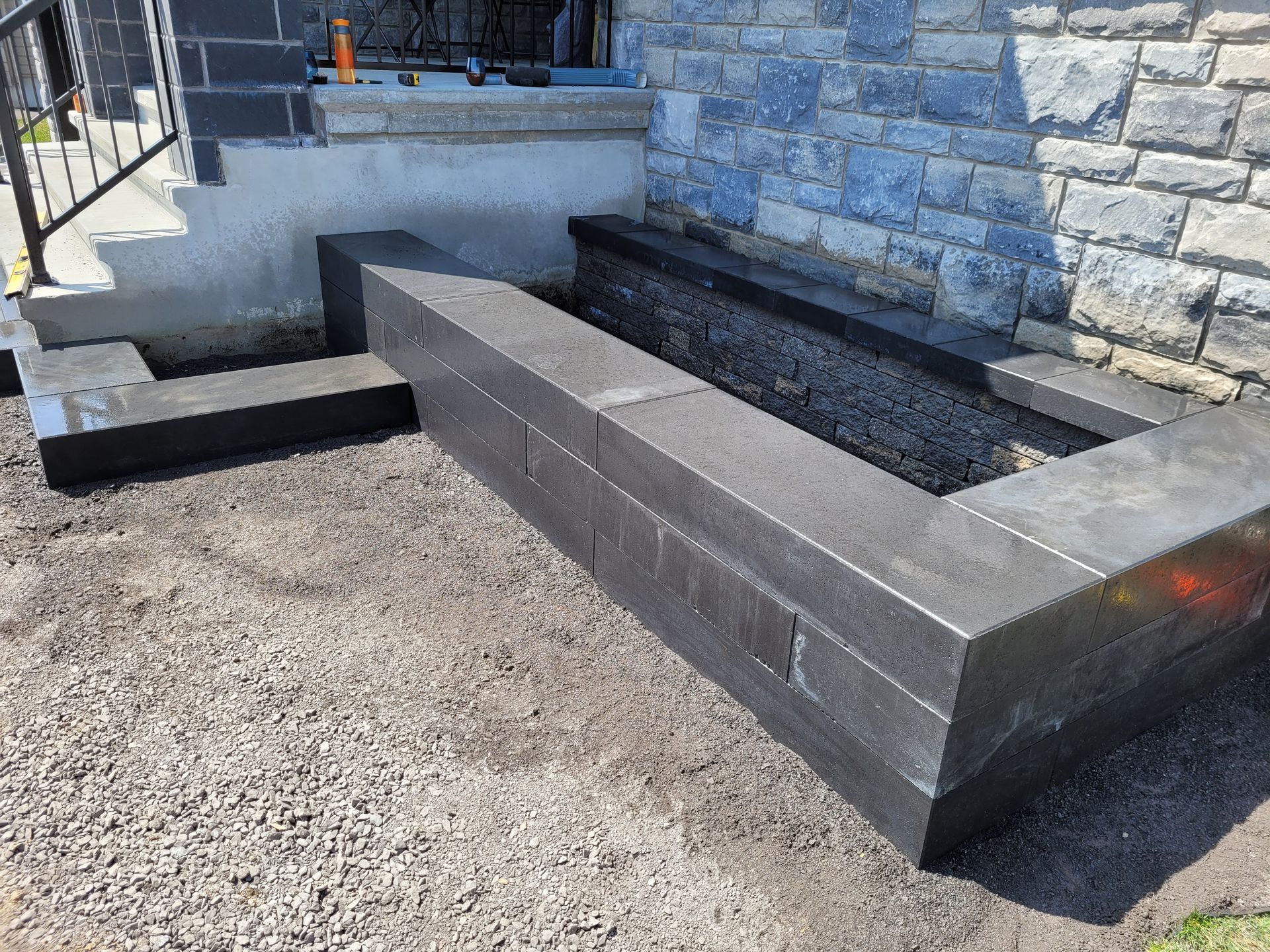 Stone planter boxes being built next to a house with stone veneer walls and a concrete staircase.