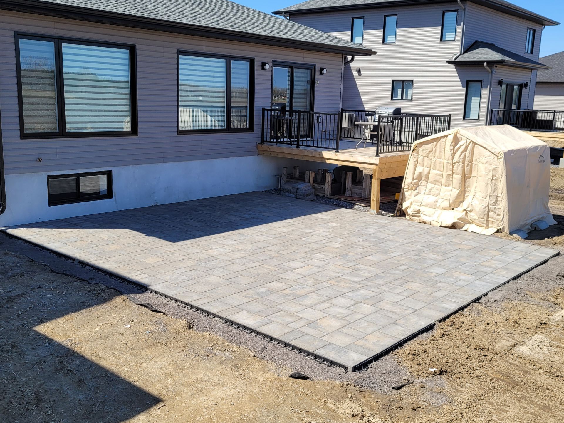 Backyard patio with brick pavers next to a house and deck, construction in progress.