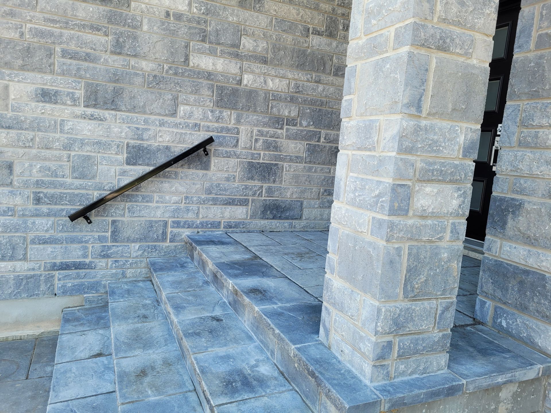 Stone steps with black handrail and stone pillar at entrance.