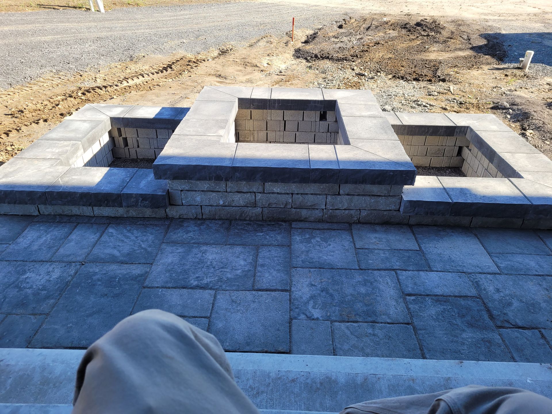 Patio en brique avec foyer carré, pierre grise, construction inachevée.