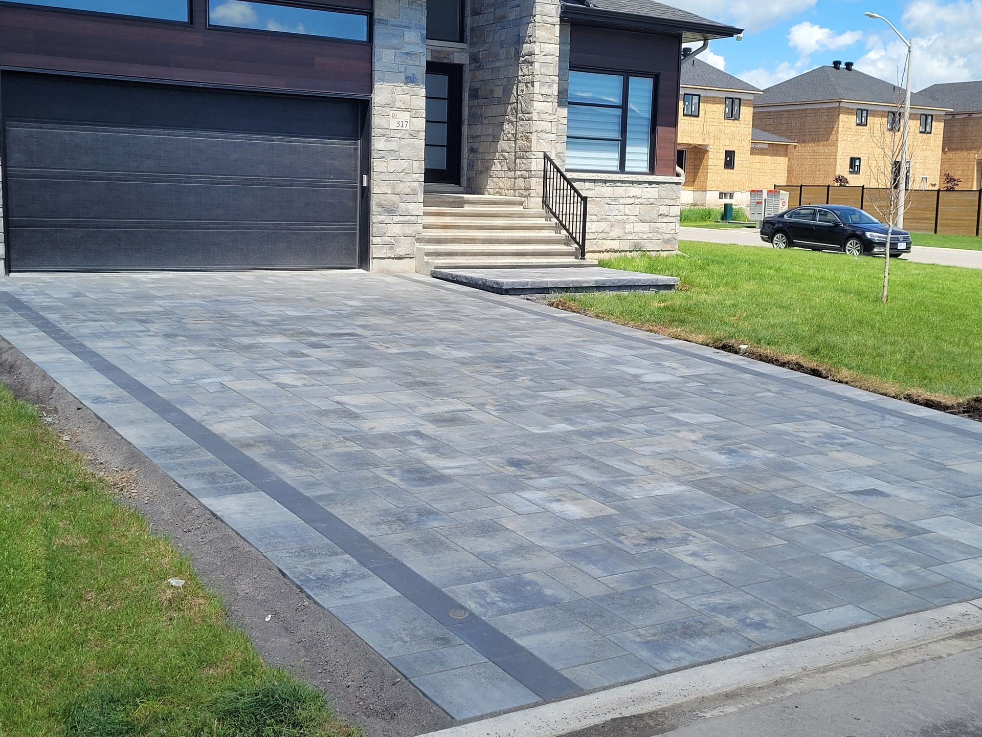 Driveway with dark gray pavers, a black garage door, and a grassy lawn.