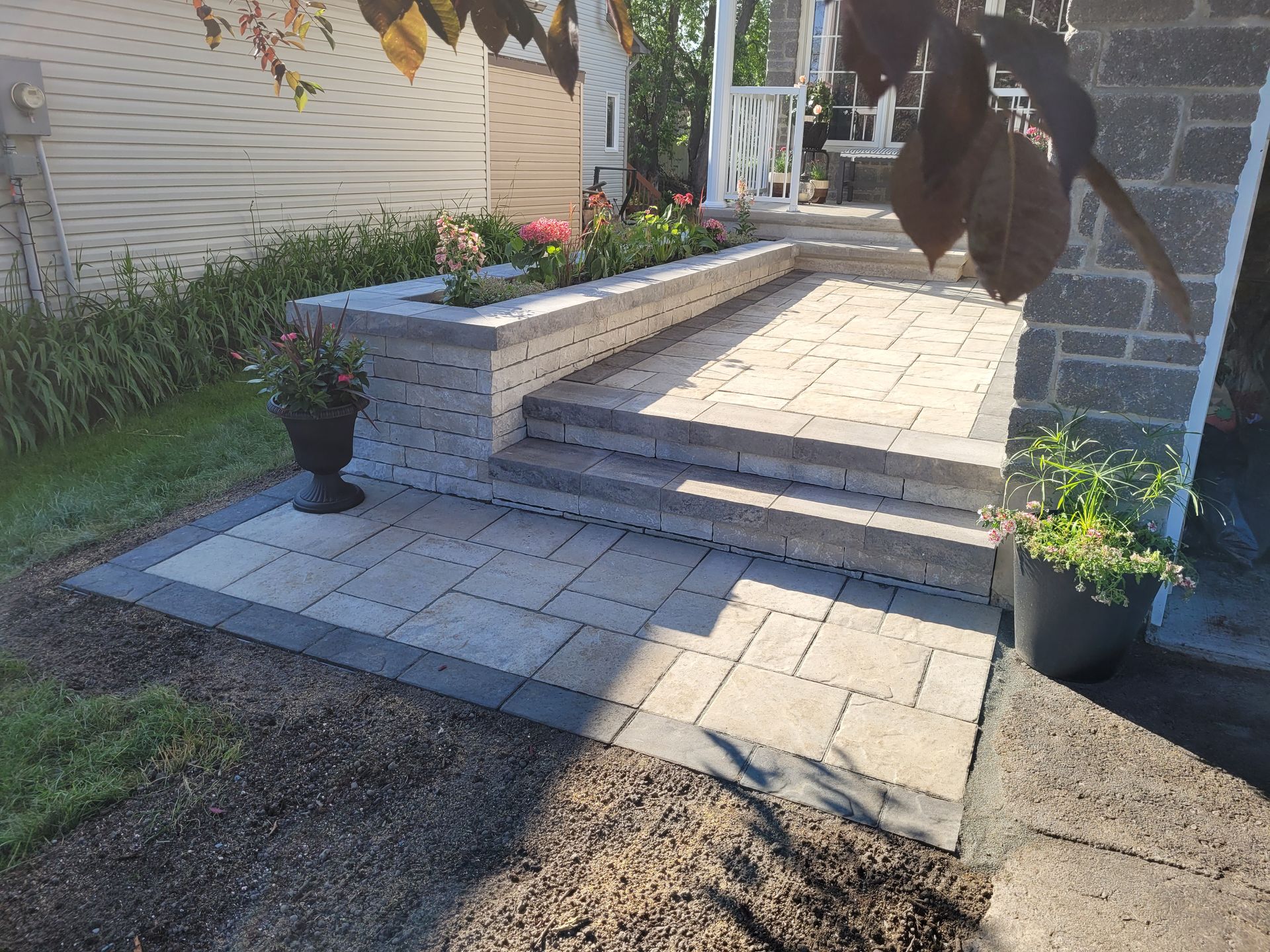 Brick patio with steps, planter, and stone facade. Light and dark gray pavers.