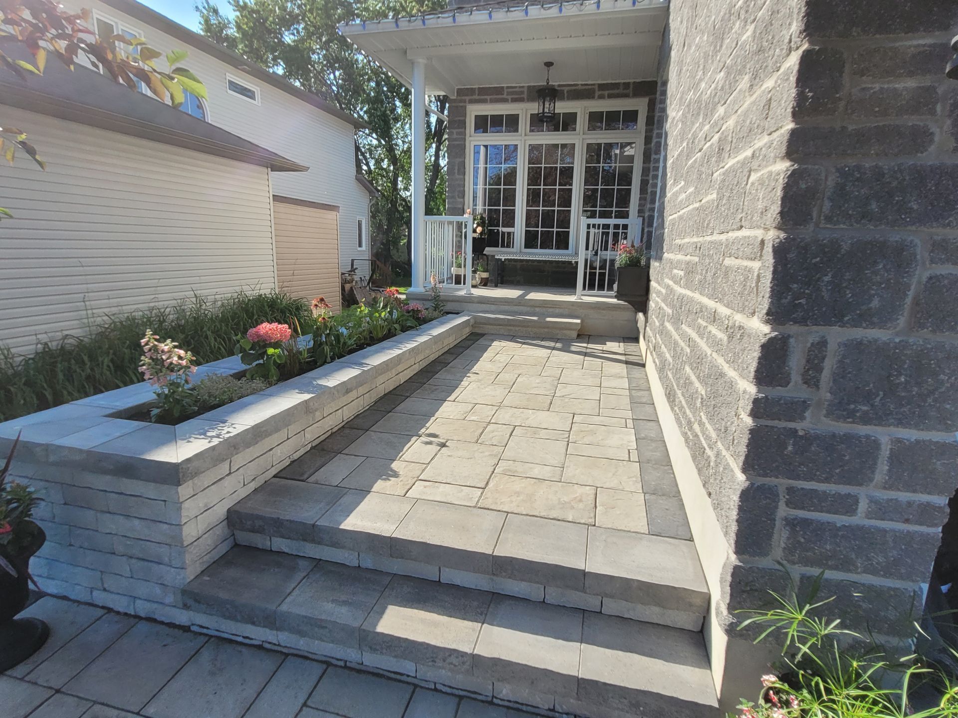 Stone walkway leading to a home's porch, with a flower bed and steps.