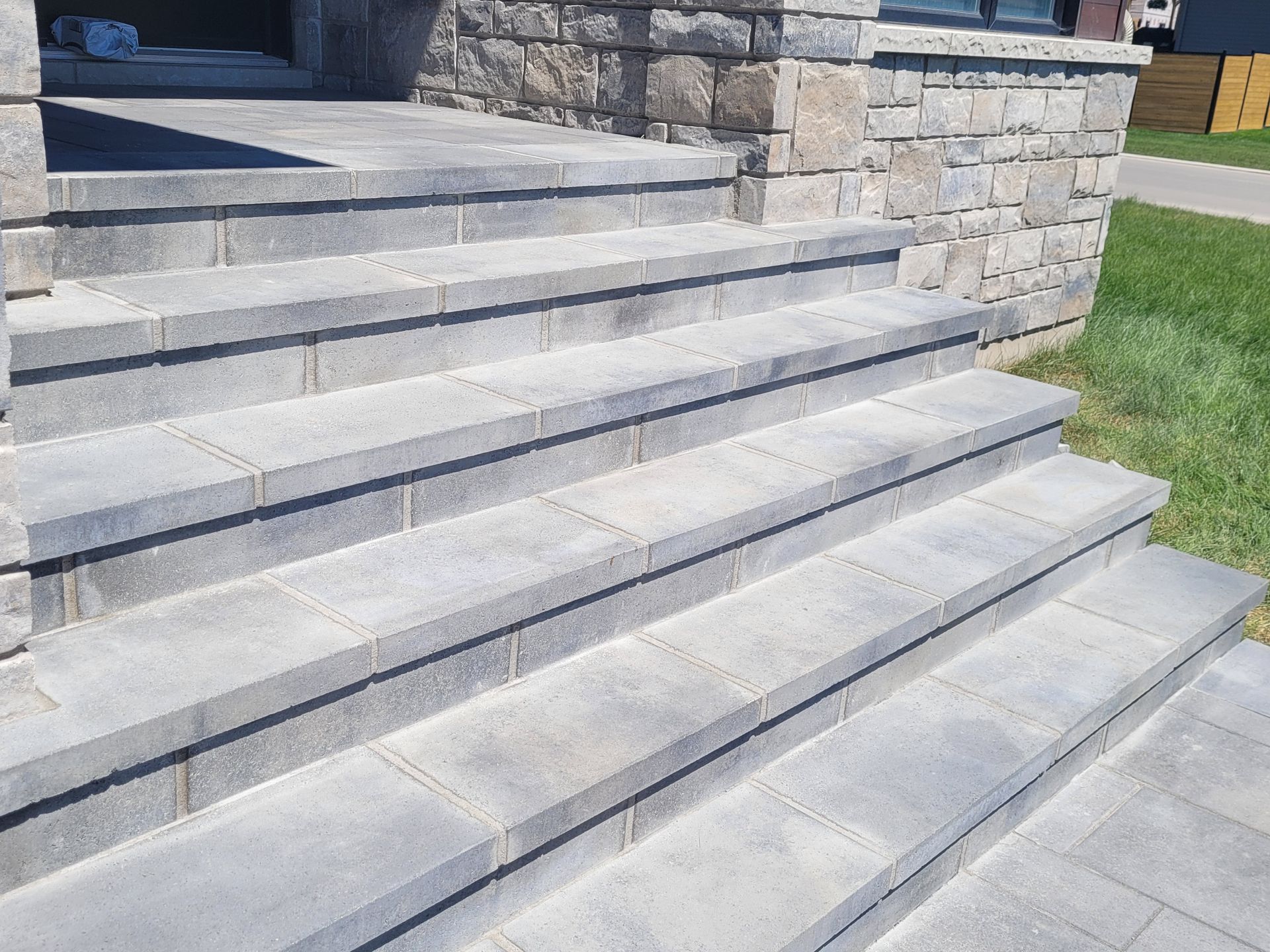 Gray stone steps leading up to a building entrance with stone facade. Sunny outdoor setting.