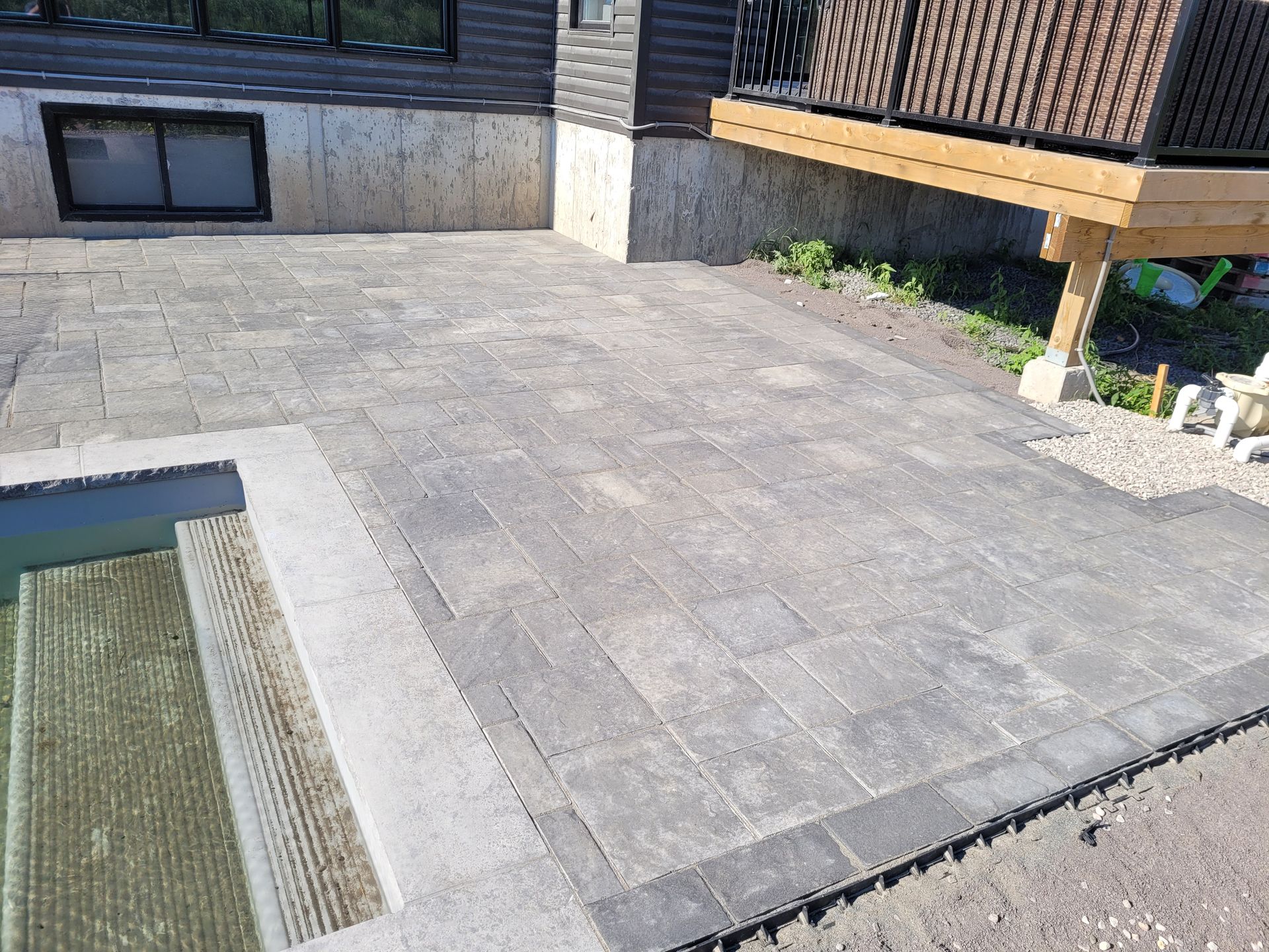 Brick patio with steps next to a building. The patio is grey, steps are wood, building is dark.