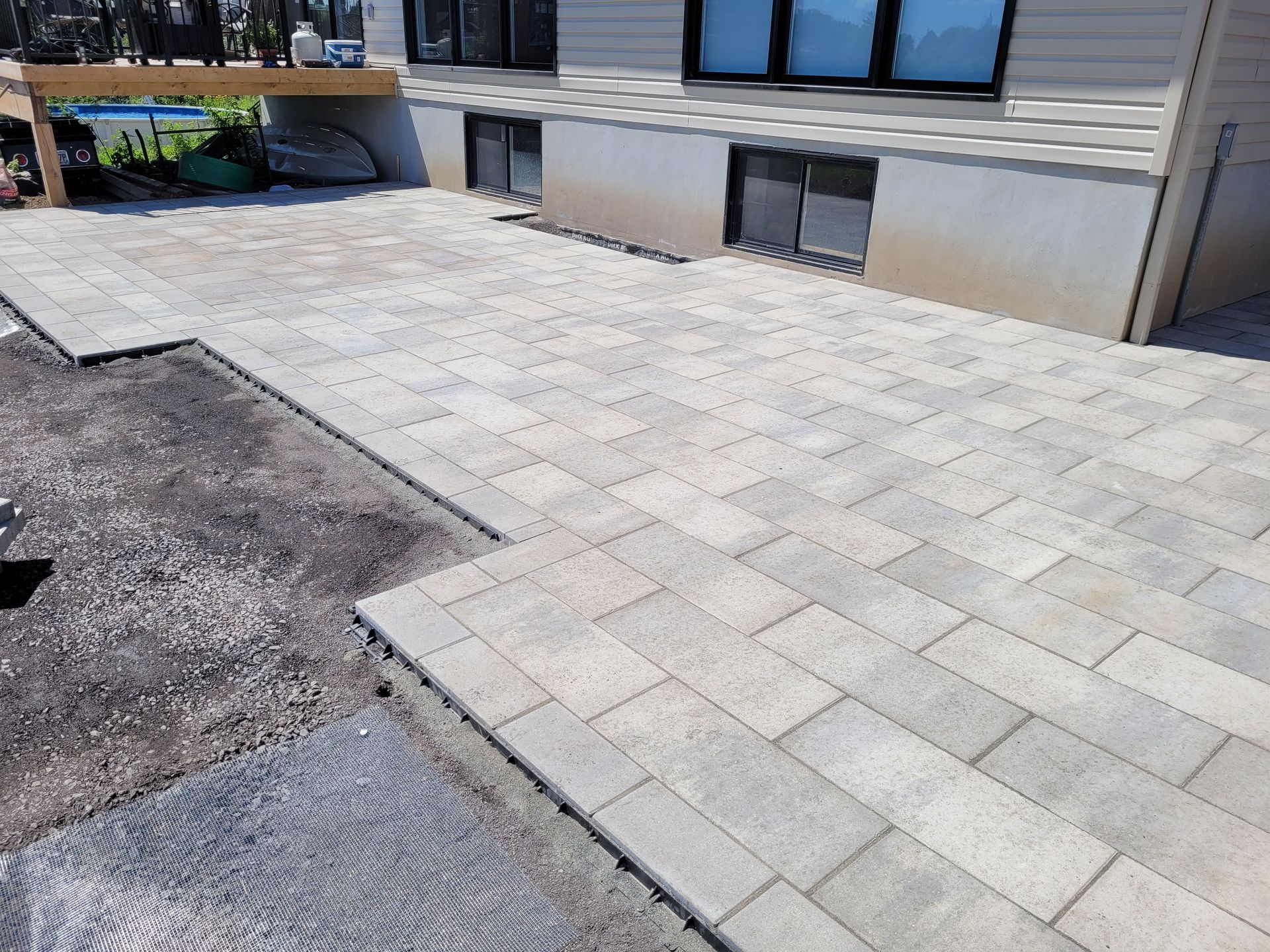 Newly paved outdoor patio with gray bricks, next to a house with basement windows.