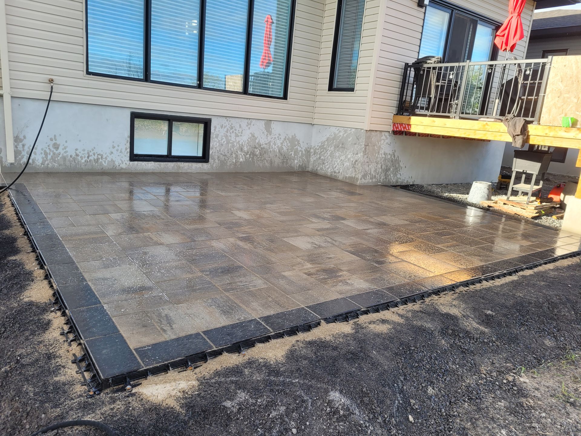 Newly laid patio with dark border, next to a house with reflective windows.