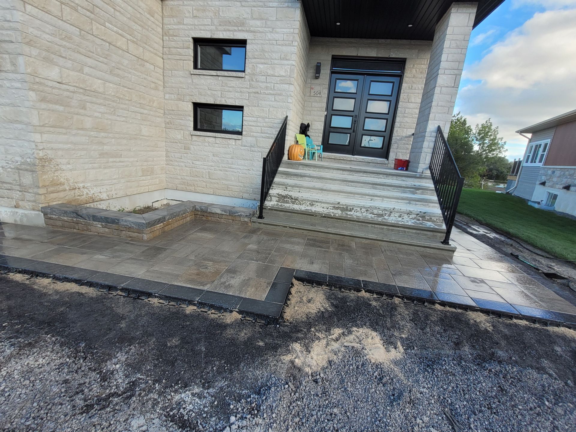 Exterior of a house with a paved walkway and steps leading to a black door. Stone facade.