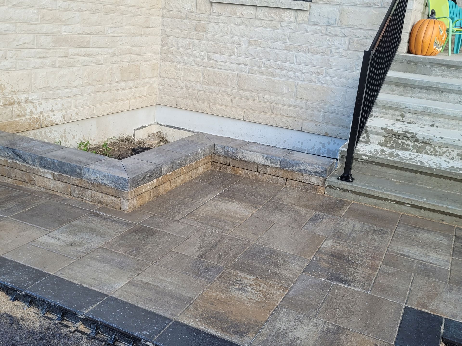 Stone patio with steps, retaining wall, and black railing. A pumpkin sits near the top.