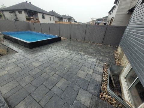 Backyard with rectangular pool, gray pavers, wooden fence, and modern house exterior.