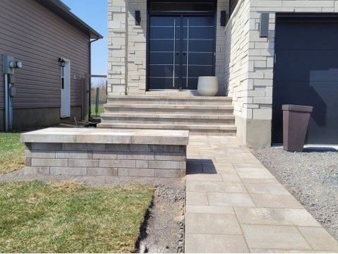 Stone walkway leads to a house with steps, a black door, and a brown trash can.